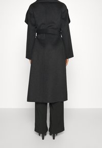 Langer schwarzer Wollmantel mit strukturiertem Kragen, tailliertem Design und weitem Ärmel, der eine glatte Textur und eine maßgeschneiderte Silhouette aufweist.