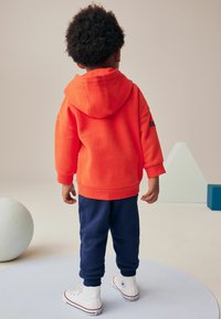 Rød hættetrøje, marineblå sweatpants, hvide høj-tops. Korte ærmer, ribbede cuffere, afslappet pasform, glat tekstur, minimal branding.