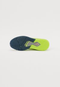 Semelle de chaussure présentant un motif de grip texturé, majoritairement jaune-vert avec une accentuation en bleu foncé. Comprend un logo gravé dans la surface.