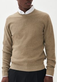 Suéter beige texturizado con un cuello redondo, puños y dobladillo acanalados, superpuesto a una camisa blanca con cuello, con un diseño de ajuste regular.