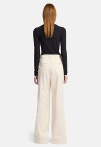 Zwarte, getailleerde top met lange mouwen, gecombineerd met een crème kleurige, hooggewande wijde broek. De broek heeft achterzakken en een soepele textuur.