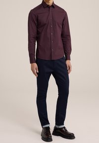 Mörkröd långärmad skjorta med knapp-up krage, bärs med marinblå byxor och mörka skor. Subtil lyster och skräddarsydd passform.