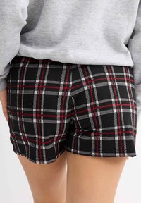 Bermudas de cuadros negros con un patrón de cuadros en rojo y blanco, textura suave y un detalle de dobladillo ligeramente deshilachado. Combinadas con una parte superior gris.
