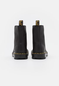 Botas de tobillo de cuero negro con un acabado suave, costuras amarillas y tiradores. Diseño elegante y suelas de goma resistente para mayor durabilidad.