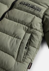 Giacca imbottita in verde oliva opaco con una texture matte, dotata di chiusura con zip, tasca laterale e logo ricamato sul petto.