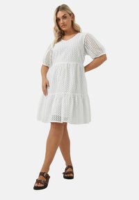 Vit midiklänning med en texturerad öppen stickning, korta puffärmar och en utsvängd nederkant. Matchad med bruna sandaler med nitar.
