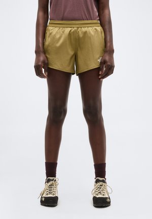 Άτομο που φοράει χακί σορτς The North Face, καφέ κάλτσες, μπεζ παπούτσια πεζοπορίας και μοβ πουκάμισο, στέκεται με τα πόδια ίσια σε λευκό φόντο.