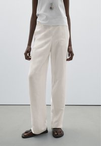 Krémové, volné lněné kalhoty s hladkou texturou. V kombinaci se světlejším topem a plochými černými sandály. Jednoduchý a univerzální design.