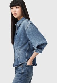 Giacca di denim azzurro chiaro con vestibilità rilassata, spalle scese e bottoni. Indossata con jeans in denim abbinati. Texture liscia, design casual.