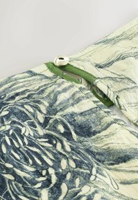 Tissu léger présentant des motifs marbrés verts et bleus. Comprend un accent métallique à la taille avec un bord en tissu.