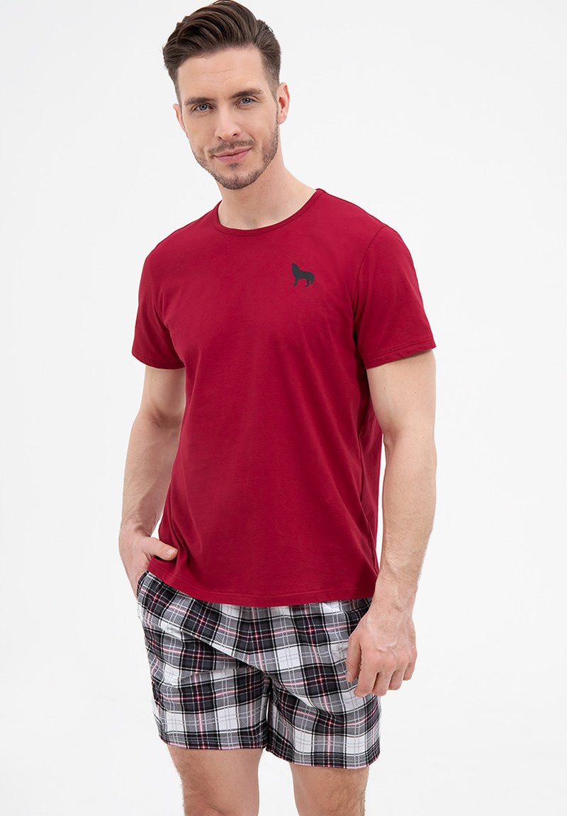 Czerwona bawełniana koszulka z krótkim rękawem i czarnym konturem psa na klatce piersiowej, w zestawie z kratkowymi szortami bokserskimi w kolorach czarnym, białym i czerwonym.