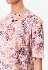 Tričko s krátkým rukávem, které má květinový potisk v odstínech broskvové, fialové a modré, s kulatým výstřihem a měkkým, lehkým materiálem.