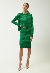 Conjunto de punto verde que incluye un top corto, un cárdigan de botones y una falda lápiz, todos con patrones geométricos y texturas contrastantes.