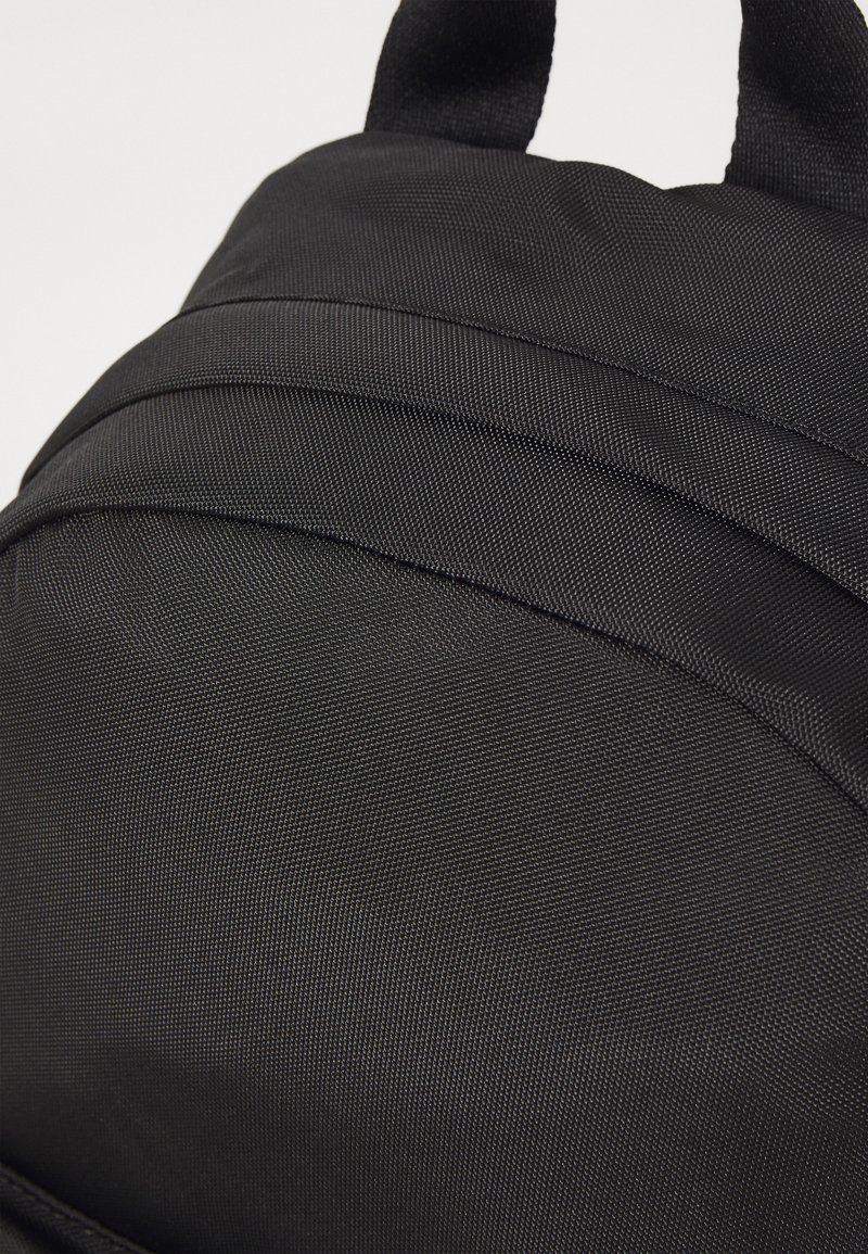 Zaino di tessuto nero con superficie testurizzata, linee pulite e due manici brevi in tessuto nella parte superiore per un facile trasporto.