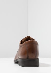 Braunes Leder-Schuh mit einer glatten Textur, flachem Design und einer schwarzen Gummisohle. Mit minimaler Nahtführung und einem eleganten Absatz.