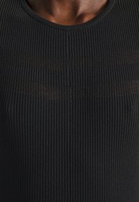 Haut noir côtelé avec un col rond, présentant de fines lignes verticales dans une texture légère. Gros plan mettant en valeur les détails du tissu.