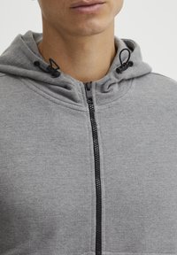Lichtgrijze sweatshirt met een rits aan de voorkant, een verstelbare capuchon met zwarte koorden en een gestructureerde stof.