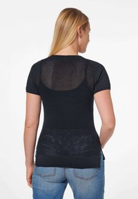 Schwarzer Kurzarm-Pullover mit strukturiertem Mesh-Rücken und festem Vorderteil. Mit gerippten Bündchen und abgerundetem Saum. Kombiniert mit hellblauen Jeans.
