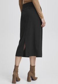 Jupe noire midi avec une fente au dos, texture lisse, taille cintrée, paire de bottines à talons en tricot marron avec des talons carrés.