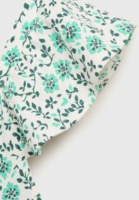 Tessuto floreale con fiori verdi e teal su sfondo bianco, caratterizzato da una texture morbida e un dettaglio di bordo arricciato.