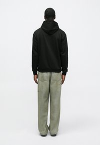 Μαύρη κου�κούλα φούτερ με υφή υφάσματος; Συνδυασμένη με ανοιχτό πράσινο παντελόνι σε γραμμή wide-leg, με φθαρμένες λεπτομέρειες και πίσω τσέπες.