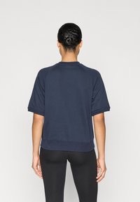 Μπλε ναυτικού κοντομάνικο φούτερ με μανίκια ράγκλαν, ριμπ τελείωμα και λεία υφή. Φορεμένο με μαύρα κολάν.