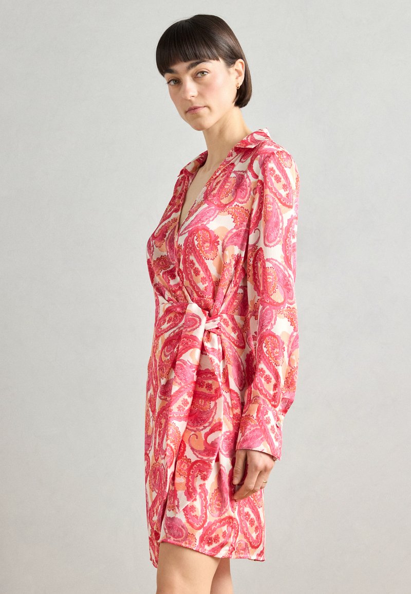 Robe portefeuille à motifs paisley roses, avec des manches longues, une ceinture à nouer et un col. Tissu doux avec une texture soyeuse. Longueur courte.