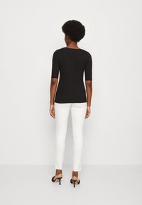 Černý fitted top s rukávy do délky loktů, doplněný bílými slim-fit kalhotami. Oblečení má minimalistický design a hladkou texturu.