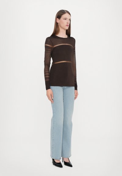Langærmet brun top med gennemsigtige stribede ærmer, parret med lyseblå jeans og sorte spidse hæle. Enkel, tætsiddende silhuet.