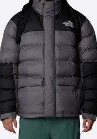 Puffig dunjacka i grått och svart med hög krage, två framfickor och The North Face-logotyp på vänster bröst. Texturerat tyg.