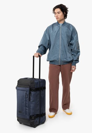 Navy fabric duffel bag with black accents, reinforced bottom, multiple zippered pockets, and a telescopic handle on durable wheels.