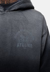 Felpa grigia scura con una gradazione sbiadita, caratterizzata da un design di farfalla e la scritta "GOOD FOR NOTHING ATELIER 1986" stampata sul davanti.