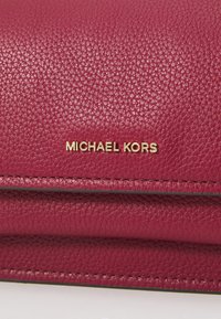 Fuksiaroosa nahast rahakott tekstureeritud viimistlusega, millel on kuldne "MICHAEL KORS" logo ja peened tikandi detailid äärealadel.