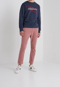Sudadera azul marino con la palabra "idéaliste" en texto rojo, combinada con pantalones de pana rosa y zapatillas blancas con una franja verde y roja.