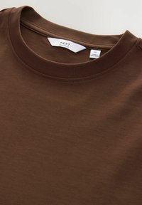 Brun kortærmet t-shirt med rund hals, lavet af glat bomuldsstof. Etiketten siger "NEXT", størrelse M, og plejeinstruktioner er inkluderet.
