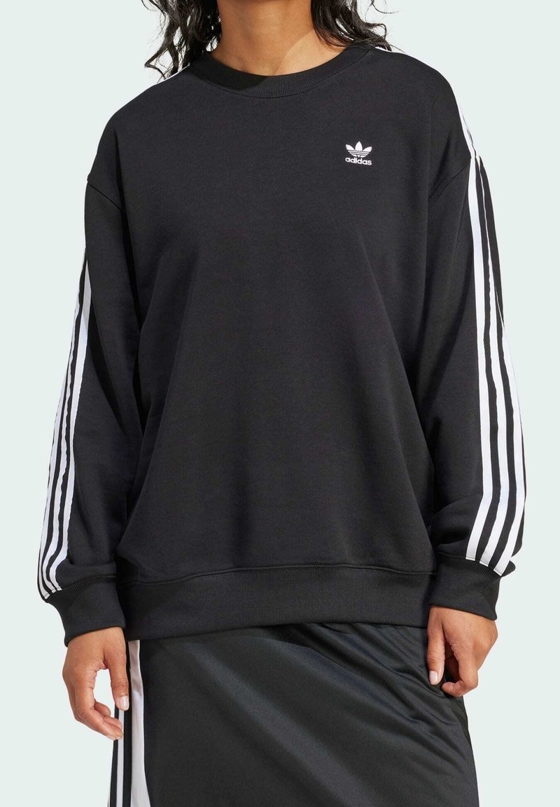 Svart sweatshirt med lös passform, vitt Adidas-logotyp på bröstet och vita tre-stripes detaljer längs ärmarna. Strukturert material.