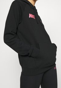 Svart hoodie i mjuk tyg, med en rosa Nike-logotyp, kenguruficka och åtsittande muddar. Slät struktur med en avslappnad design.