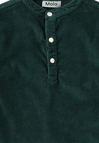 Tumma vihreä corduroy-paita, jossa on pyöreä pääntie, viisi pientä valkoista nappia ja hienovarainen rakenne. Tunnuksessa lukee "Molo."