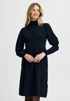 Navyblaues Strickkleid mit hohem Kragen, puffärmeligen Ärmeln und einer taillierten Oberseite, die sich an der Taille ausstellt, mit einer glatten, weichen Textur.
