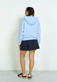 Jasnoniebieska bluza z kapturem na sznurku, w połączeniu z ciemnogranatową plisowaną spódnicą. Brązowo-kremowe sneakersy dopełniają stylizację.