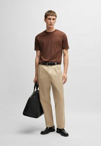 T-shirt corto marrone a maniche corte, pantaloni beige, cintura nera, borsa nera e scarpe nere. Design minimalista, texture liscia, colori neutri.