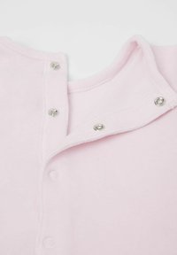 Różowy bawełniany kombinezon z zapięciem na napy, z okrągłym dekoltem oraz miękkim, teksturowanym materiałem. Udoskonalony metalicznymi napami.