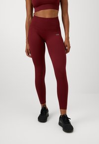 Høytlivete, ribbet leggings i burgunder med bred midjebånd, paired med en matchende crop topp. Svarte treningssko fullfører antrekket.