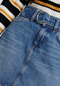 Džínová sukně s světle modrým umytím, se zaobleným stříbrným přezkou na opasku, s prošitými detaily a předními kapsami. Pruhovaný svetr viditelný nahoře.