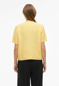 Žlutý krátký pletený svetr s kulatým výstřihem a žebrovaným lemem, zobrazený zezadu na jednoduchém bílém pozadí.