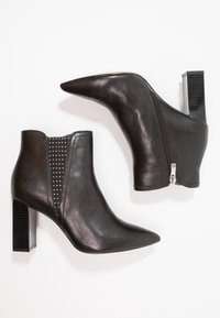 Botas de tobillo de cuero negro con punta afilada, cremallera lateral y tacón bloque acanalado. Presentan un panel de tela con puntos a los lados.