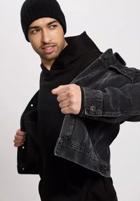 Czarna dżinsowa kurtka z zapięciem na guziki z przodu, noszona na czarnej bluzie z kapturem. Kurtka ma klasyczny kołnierz i szczegółowe przeszycia.