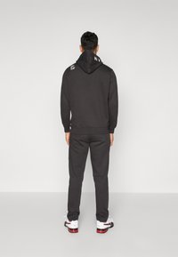 Sort hættetrøje med snoretræk og logo-detalje, parret med matchende joggers. Outfittet har en afslappet pasform og en glat tekstur.