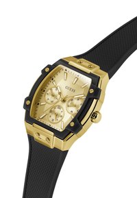 Un elegante orologio Guess con quadrante rettangolare dorato, dotato di più indicatori e di un cinturino in gomma nera. Design elegante e moderno.