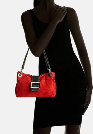 Rood suède handtas met een zwarte leren schouderband en gespdetails. De tas heeft zilveren hardware en een ritsafsluiting.
